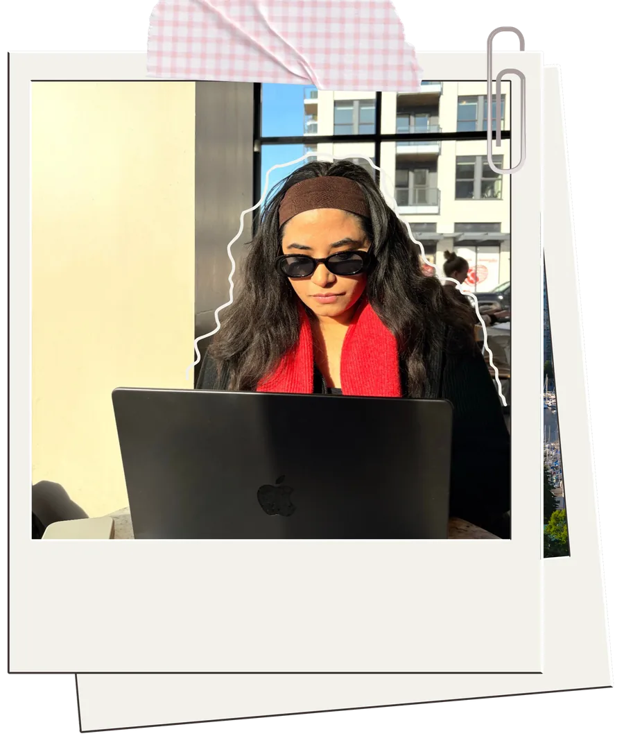 Polaroid photo of Manmit in sunglasses and a red scarf, working on a laptop by a window